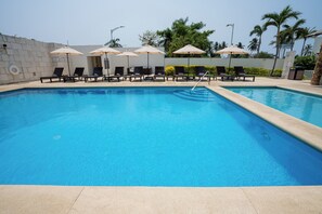 Una piscina con sillas de descanso y sombrillas, rodeada de un muro de piedra y palmeras.