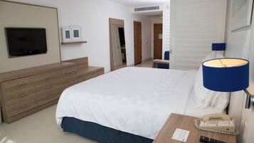 A hotel room with a bed, a TV mounted on the wall, a bedside table with a lamp, a phone, and a remote control.