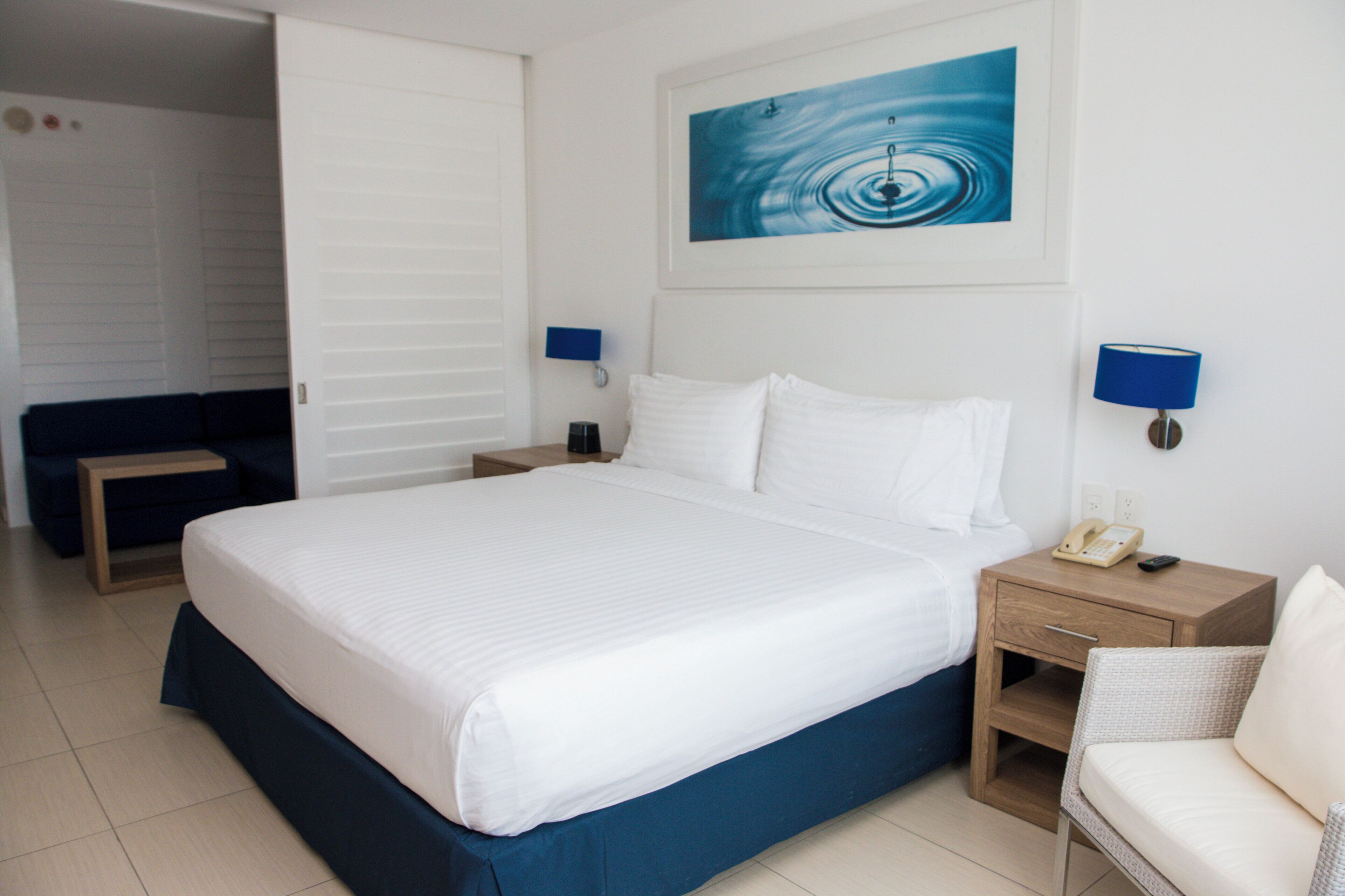 A hotel room with a large bed, bedside tables, a chair, and a painting on the wall.