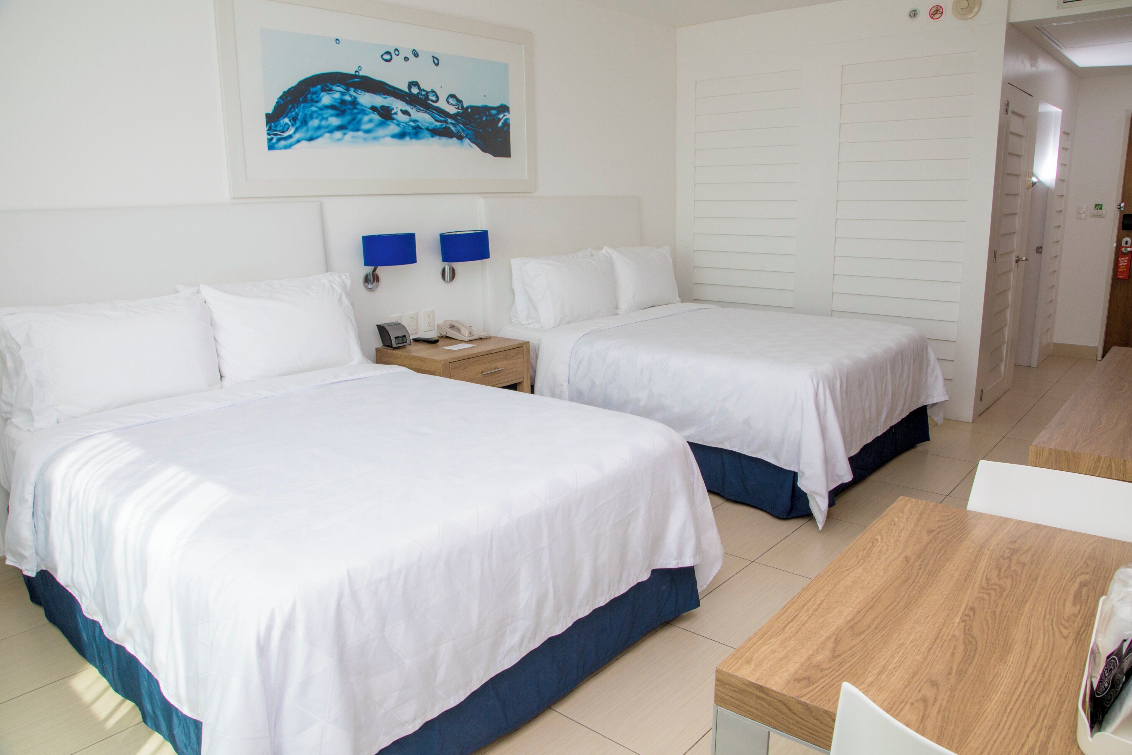 Une chambre d’hôtel avec deux lits, une table en bois, une table de chevet et un tableau au mur.