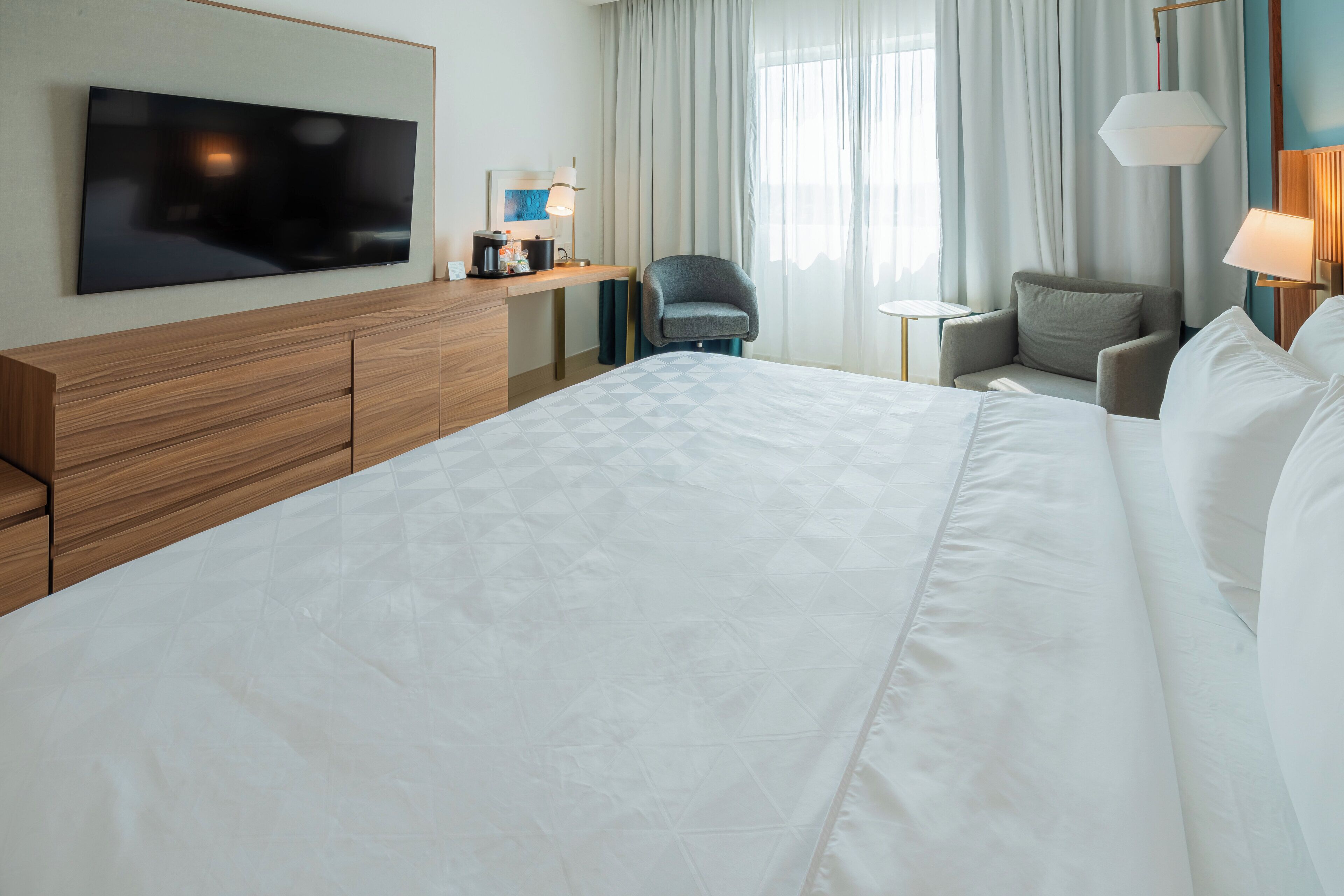 Camera d'albergo con un letto grande, una TV a parete, una scrivania con una lampada, due poltrone e un tavolino.