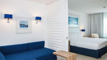 Habitación de hotel con sofá azul, mesita de madera, cama con ropa de cama blanca y dos lámparas fijadas a la pared.