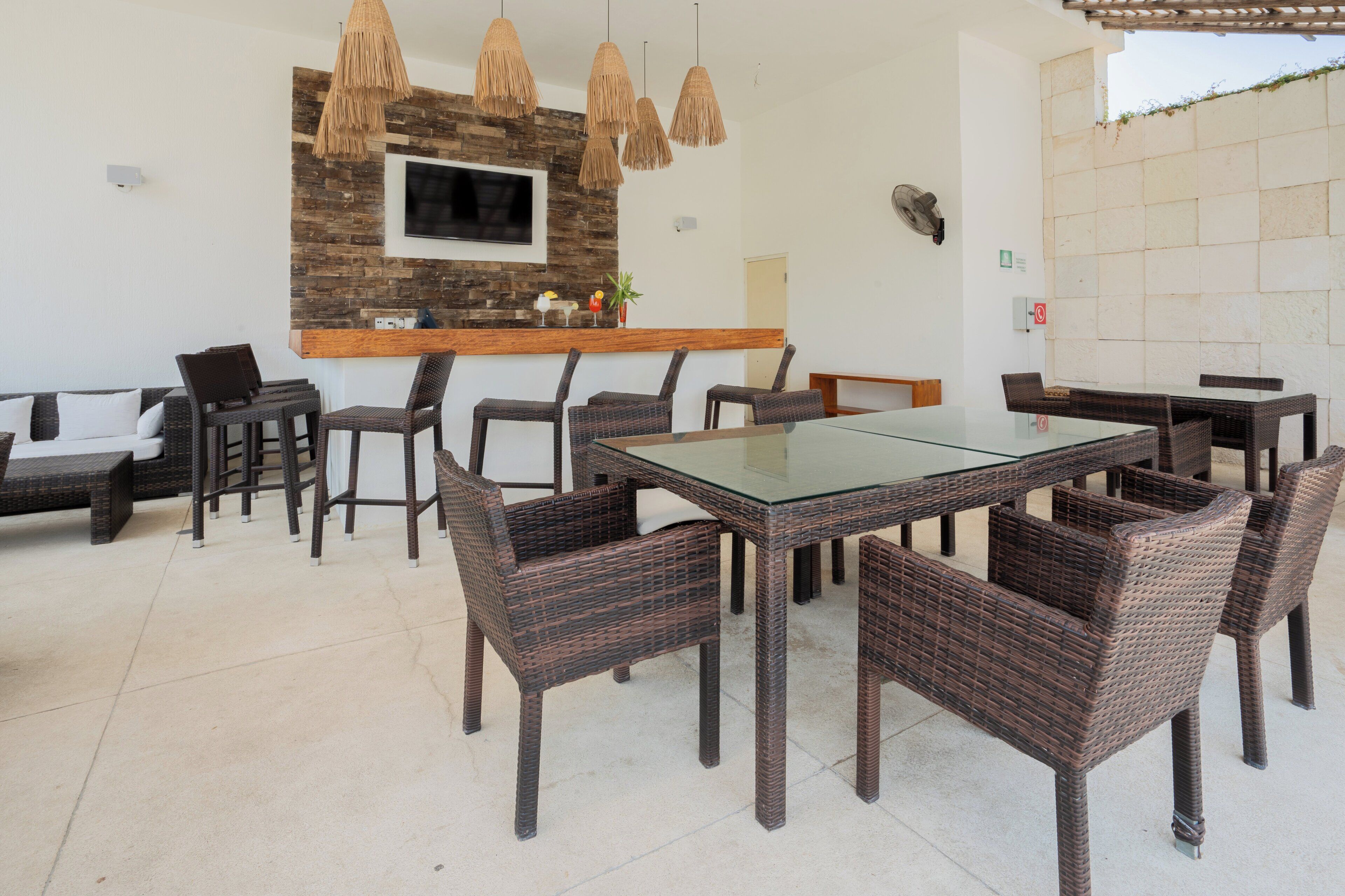 An outdoor dining area with wicker furniture, a glass-top table, and hanging pendant lights.