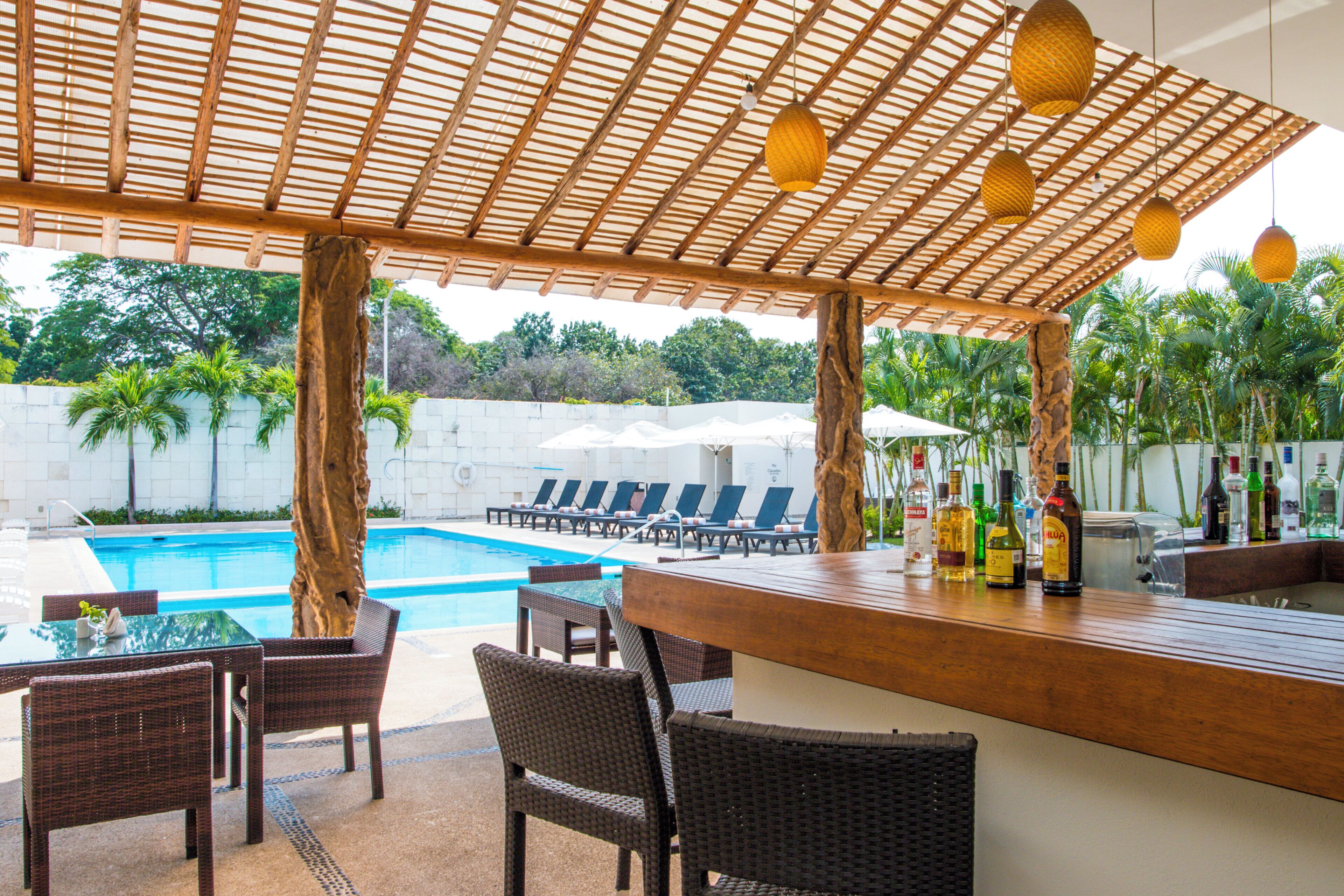 A poolside bar area with wicker furniture, a pool, and lounge chairs.