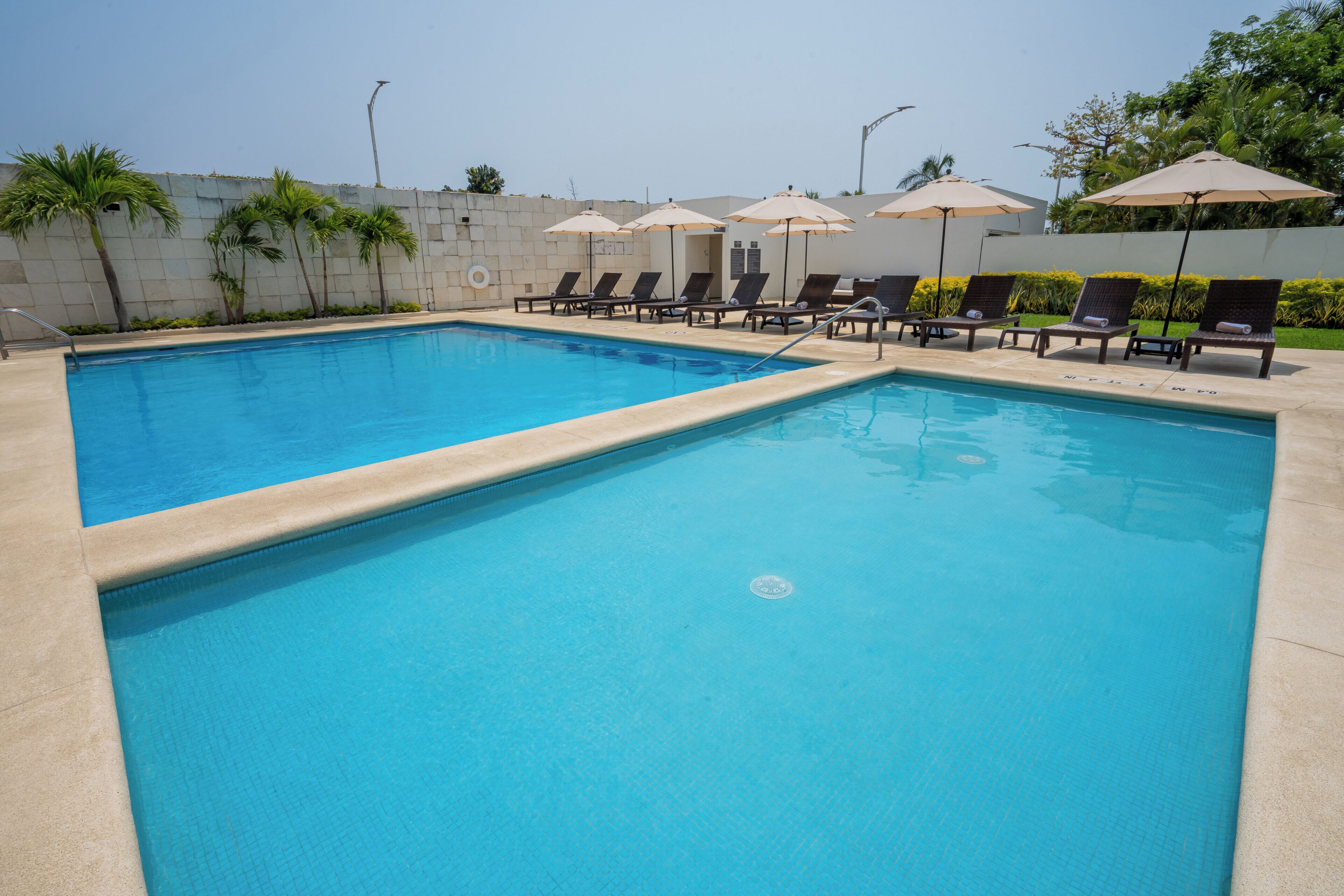 A rectangular swimming pool with clear blue water, surrounded by lounge chairs and umbrellas.