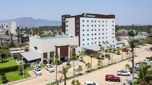 Un hotel Holiday Inn con diseño moderno, que presenta un techo plano y un estacionamiento con varios coches.