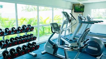 Un gimnasio con equipo de ejercicio, un televisor y una ventana con vistas a zonas verdes.