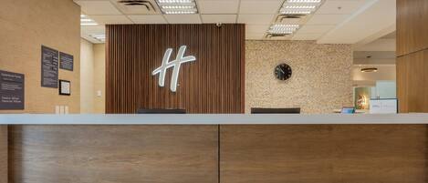 Un comptoir d’accueil avec un panneau en bois et un grand logo « H » lumineux.