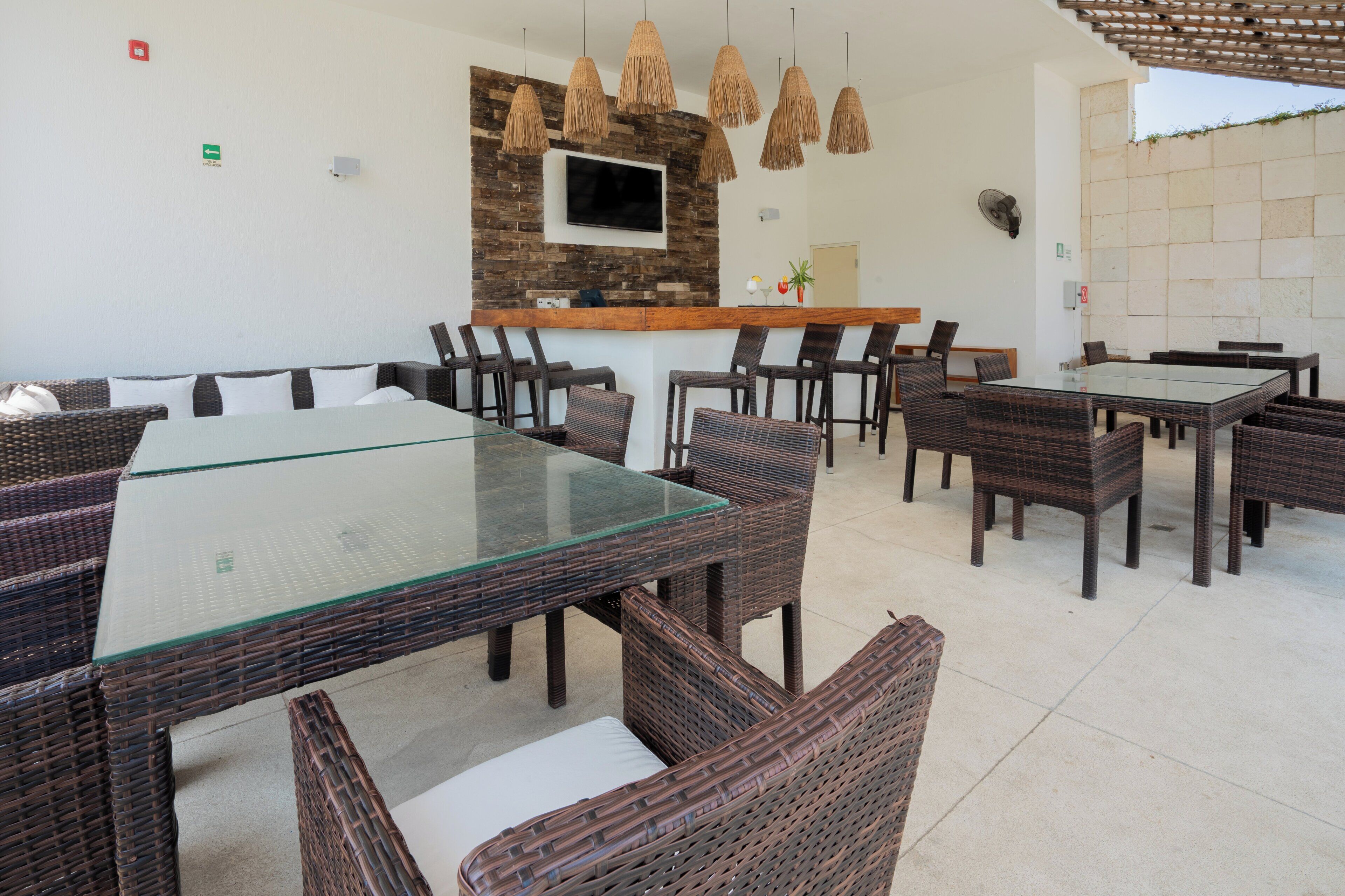 Un comedor con mobiliario de mimbre, una mesa de vidrio y una pared de piedra con un televisor.