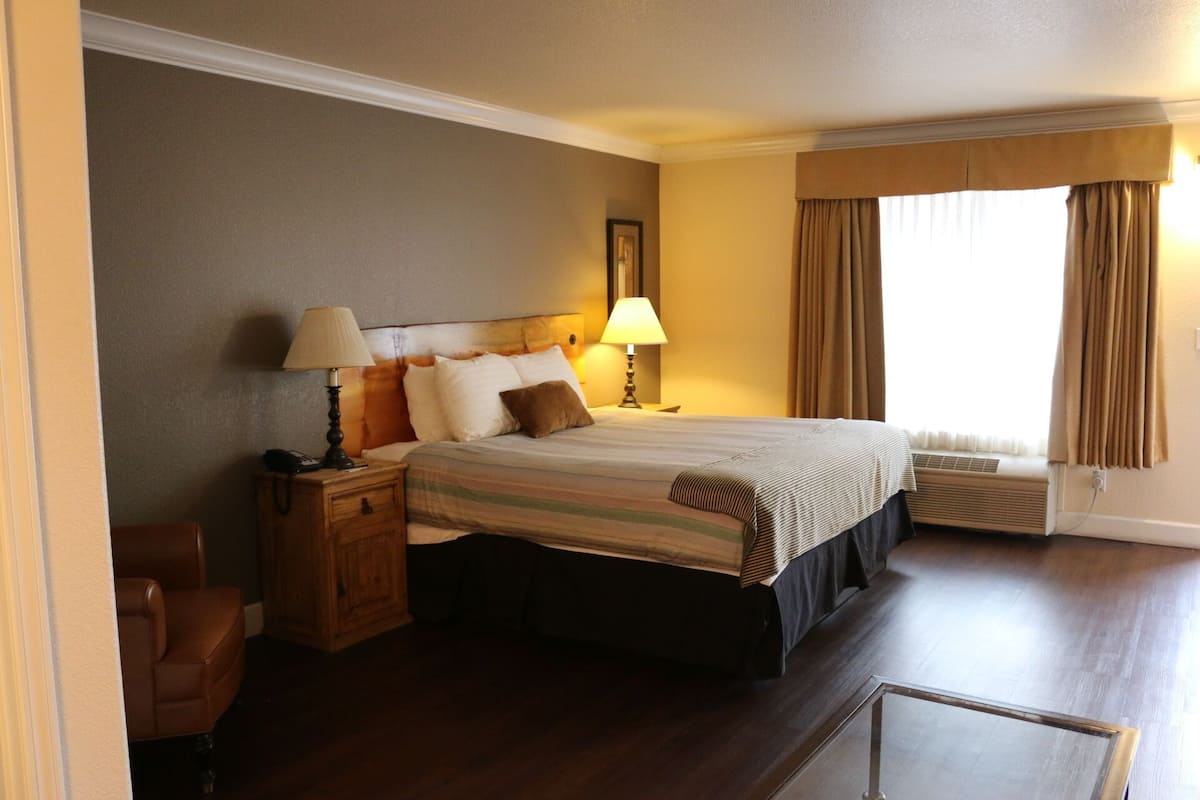 Une chambre d’hôtel avec un grand lit, deux lampes de chevet, une table de chevet en bois, une chaise et une fenêtre avec des rideaux.