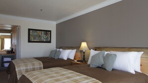 Habitación de hotel con dos camas, una mesita de noche con lámpara, un cuadro en la pared y un escritorio con espejo y cafetera.