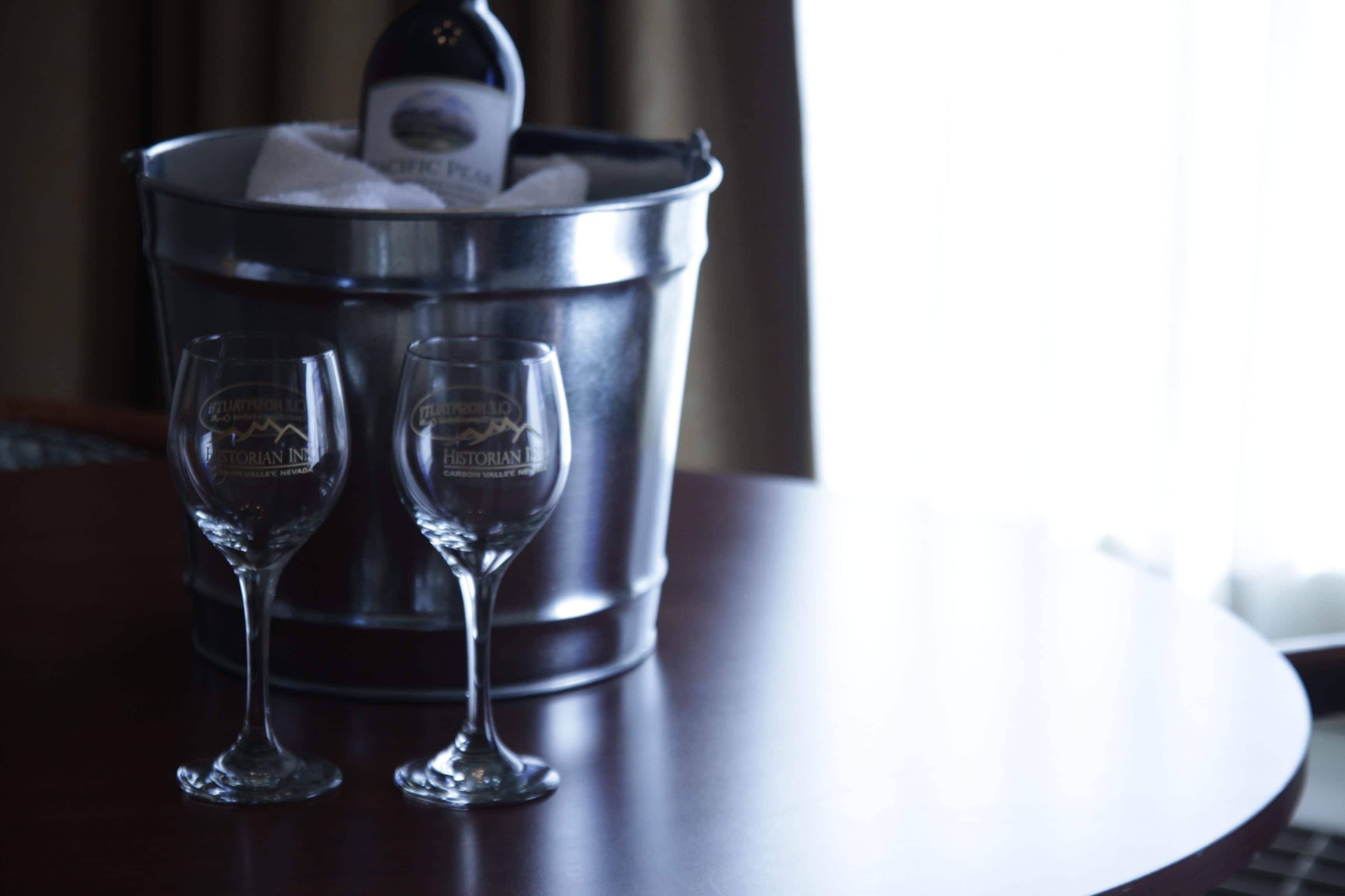 A metal bucket with two empty wine glasses and a bottle of wine.