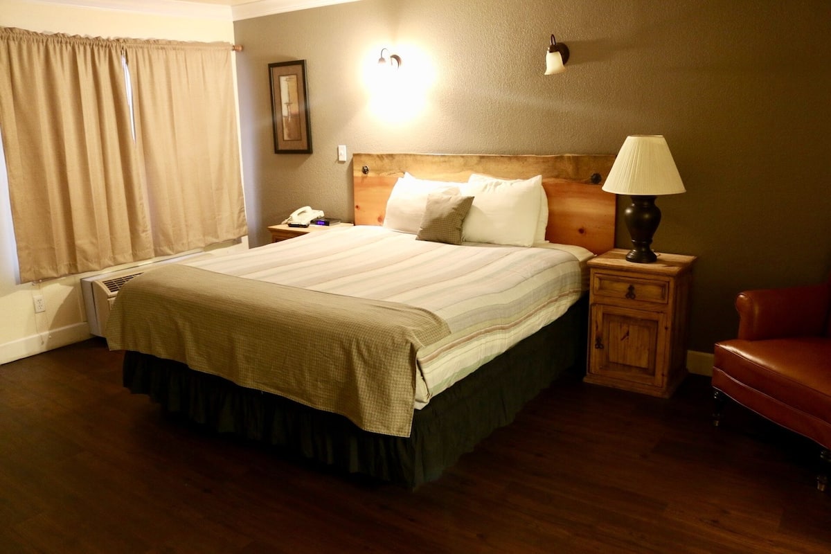 Une chambre d’hôtel avec un grand lit, une table de chevet, une lampe, une chaise et un luminaire fixé au mur.