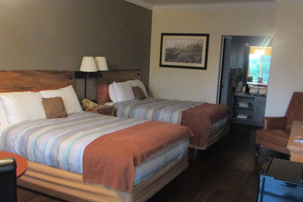 Une chambre d’hôtel avec deux lits, un bureau, une chaise et un tableau encadré au mur.