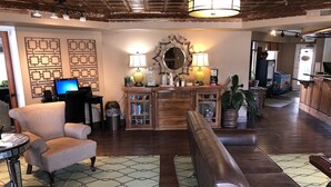 Amplia sala de estar con un sofá de cuero, una mesa de centro redonda y un televisor. Se observa un mueble de madera con libros y objetos decorativos, además de una alfombra estampada en el suelo.