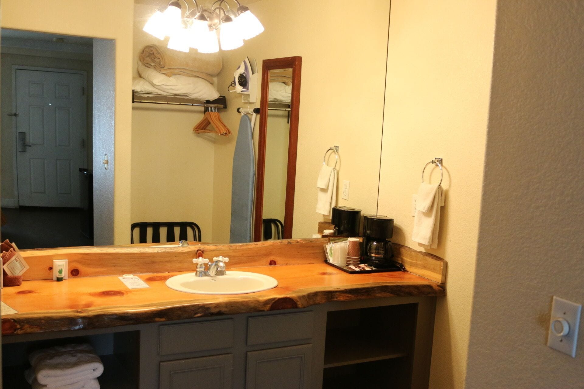A bathroom with a wooden vanity, a sink, a mirror, and a coffee maker.