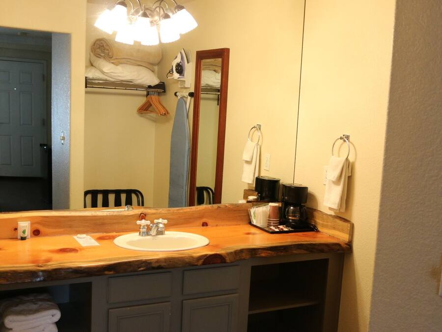 A bathroom with a wooden vanity, a sink, a mirror, and a coffee maker.