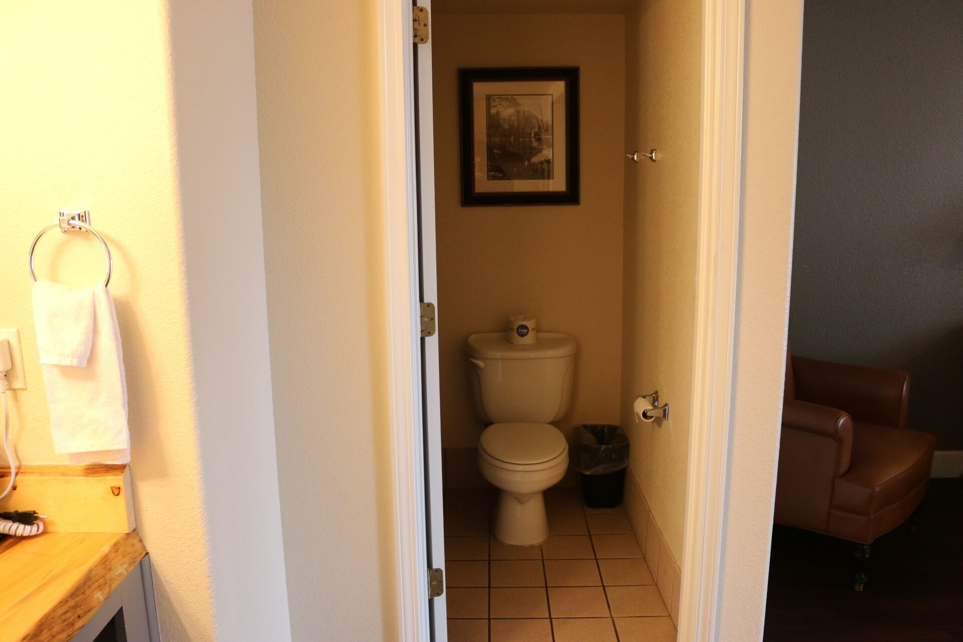 Une petite salle de bain étroite, avec des toilettes, une poubelle et un tableau encadré accroché au mur.