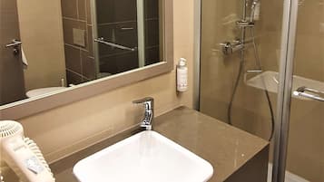 A bathroom with a glass-enclosed shower, a white sink, a mirror, and a hairdryer on the countertop.
