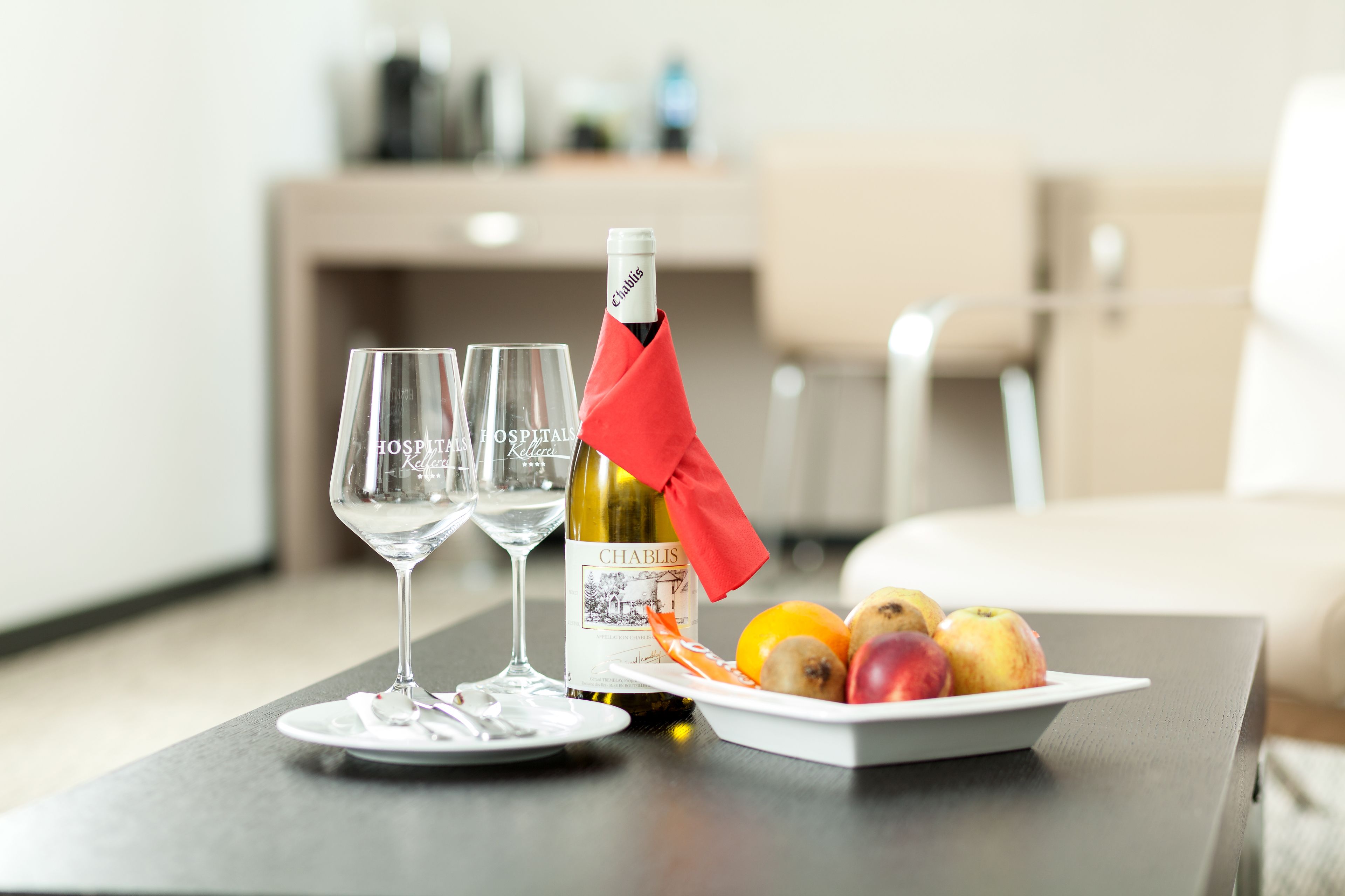 A table with a bottle of wine, two glasses, and a plate of fruit.