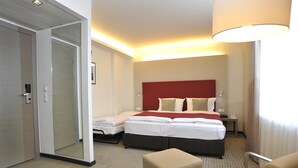 A hotel room with a bed, two bedside tables, a desk, a chair, and a door. - Golden Tulip Kassel Hotel Reiss (Kassel)