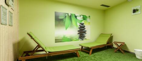 Una habitación con dos sillones de madera, una pared verde, un cuadro de una fuente de agua y una pequeña mesa de madera.