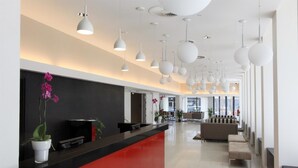 A modern reception area with a black and red counter, white pendant lights, and a seating area with a sofa and chairs. - Golden Tulip Kassel Hotel Reiss (Kassel)