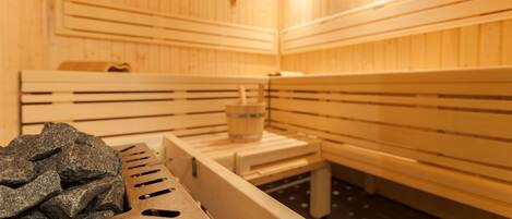Una sauna amb seients de fusta i un banc amb una tovallola i un cubell.