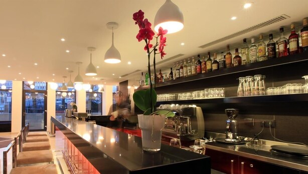 A modern bar area with a long counter, overhead pendant lighting, and a variety of liquor bottles on shelves. - Golden Tulip Kassel Hotel Reiss (Kassel)