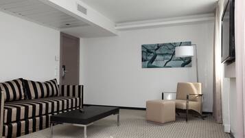 A hotel room with a striped sofa, a small table, a beige armchair, and a painting on the wall.