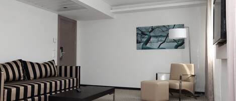 Una habitación de hotel con un sofá a rayas, una mesita, un sillón color beige y un cuadro en la pared.