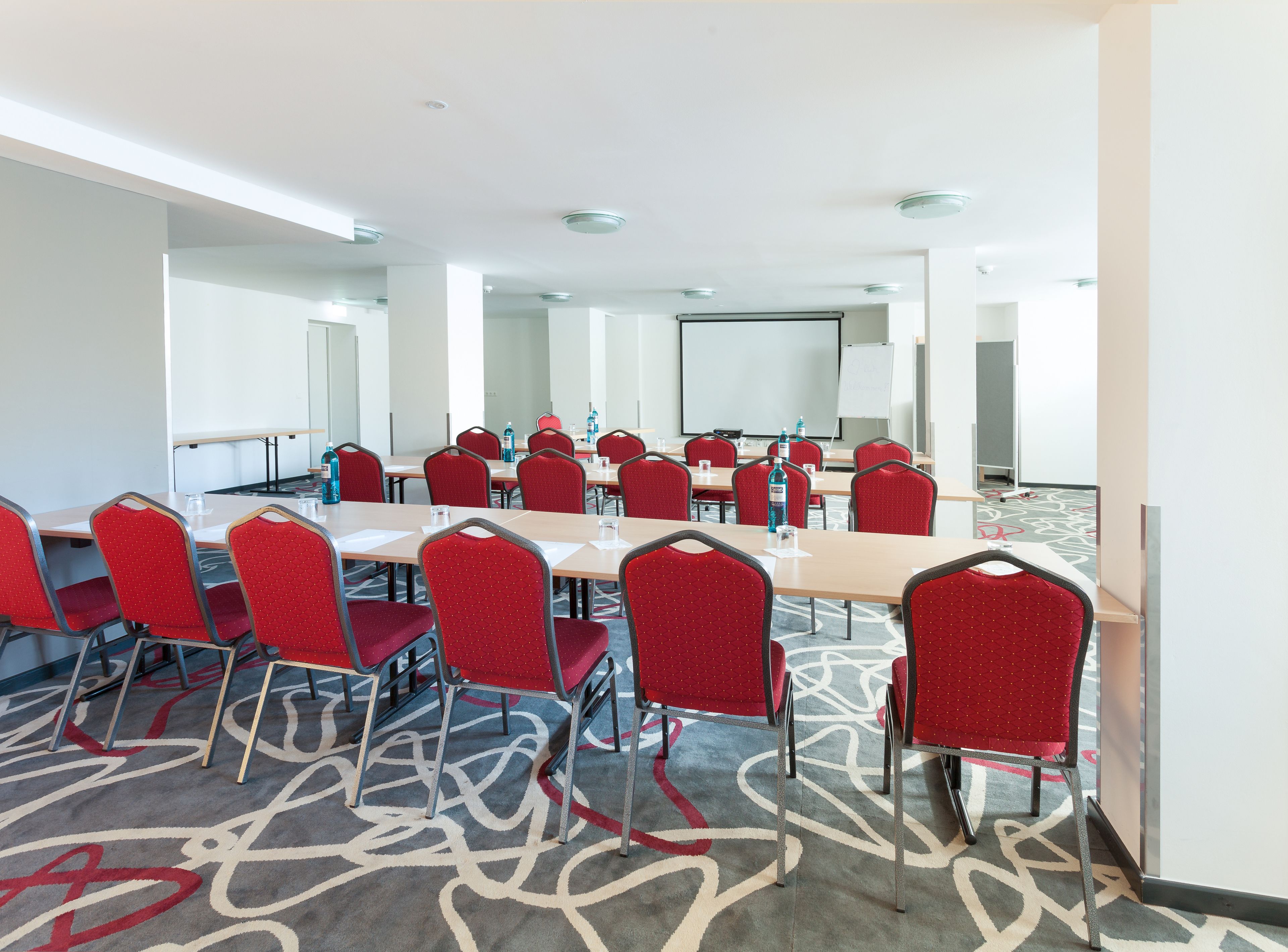 Une salle de conférence avec des chaises rouges, une grande table et un écran de projection.