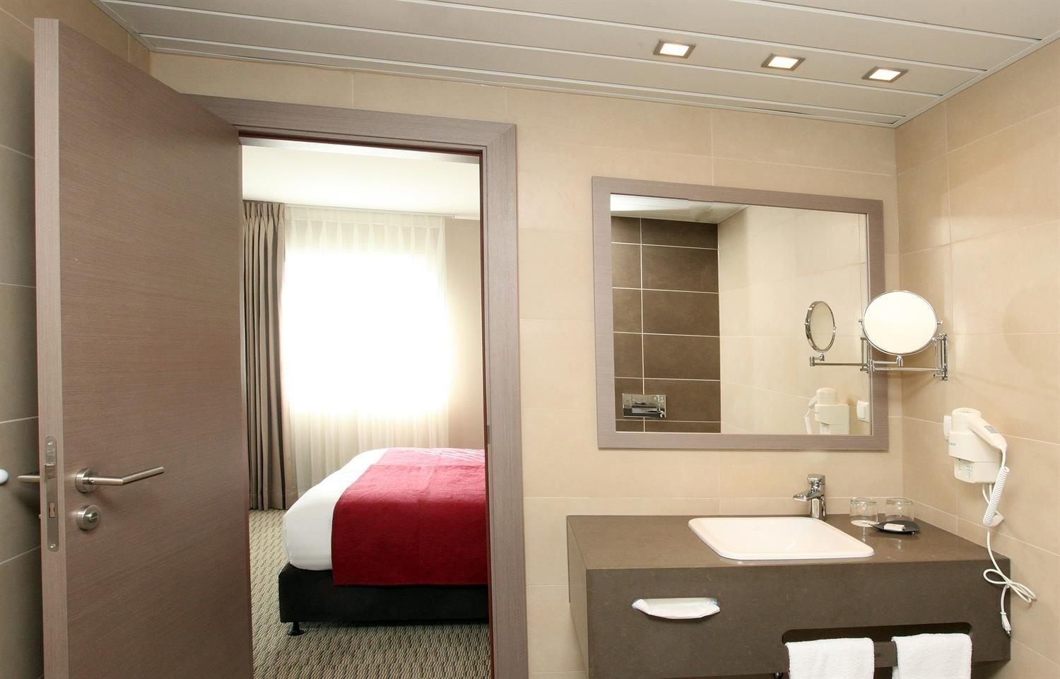 A hotel room with a bed, a bathroom with a sink, mirror, and hairdryer.