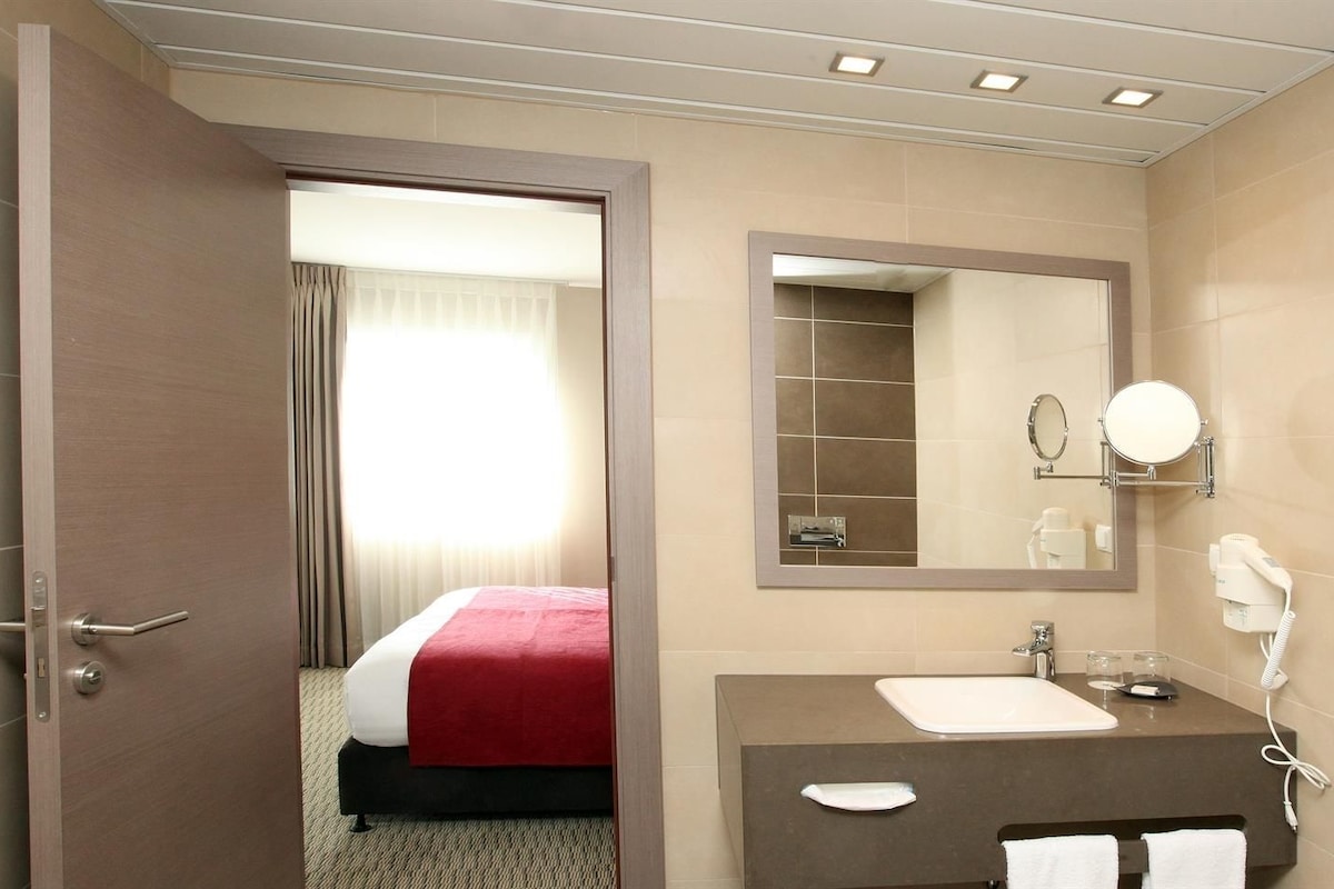 Een hotelkamer met een bed en een badkamer met wastafel, spiegel en haardroger.
