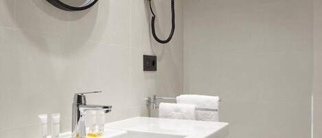 A modern bathroom with a large mirror, two sinks, a hairdryer, and a toilet.