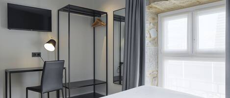 Ein modernes Hotelzimmer mit einem Bett, einem Schreibtisch mit Stuhl, einem Fernseher und einem großen Fenster mit Vorhängen.