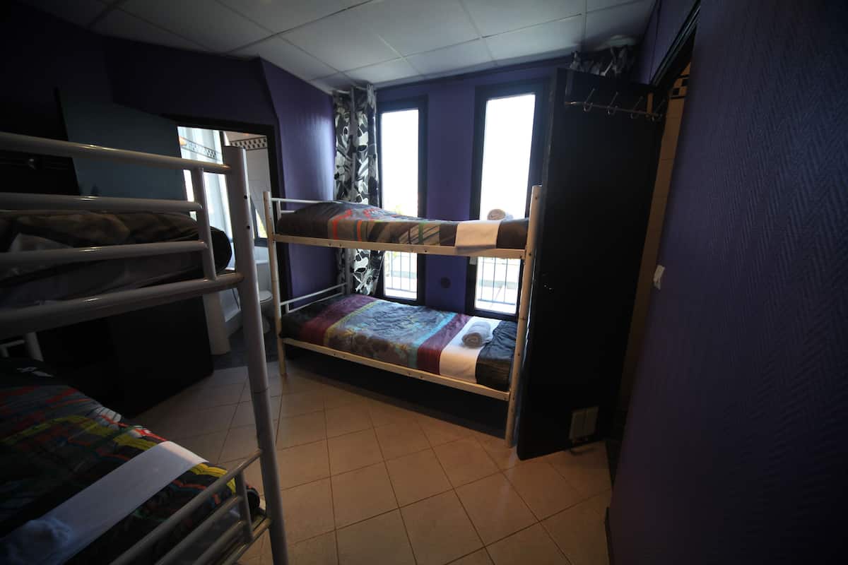 A dormitory room with bunk beds, a window, and a door.