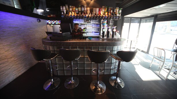Una zona de bar con un cantinero, taburetes y una estantería repleta de licores.