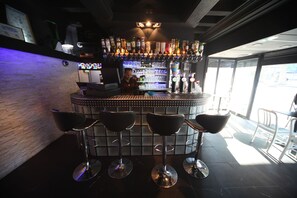 A bar area with a bartender, bar stools, and a well-stocked liquor shelf. - Peace & Love - Hostel (Paris)