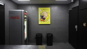 Un baño con un refrigerador Coca-Cola, dos botes de basura y un cartel llamativo en la pared.