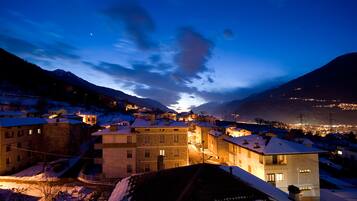 A snow-covered town at dusk with illuminated buildings and mountains in the background.