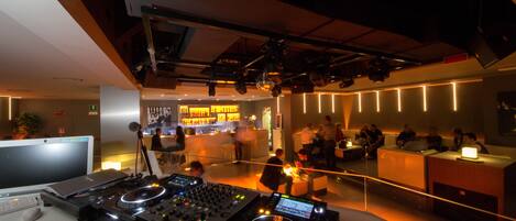 A modern bar area with DJ equipment, seating, and a bar counter.