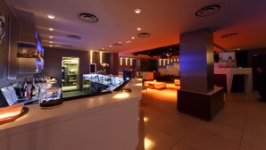 Un área de bar moderna con mostrador, estanterías llenas de botellas y una zona de estar con mesas y sillas.