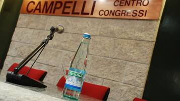 A bottle of Levissima water on a table with a microphone stand and a sign reading "Campelli Centro Congressi".