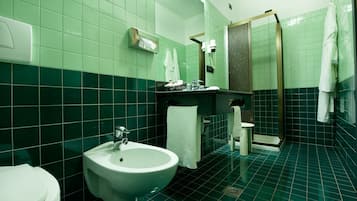 A bathroom with a bidet, a sink, a mirror, and a shower.