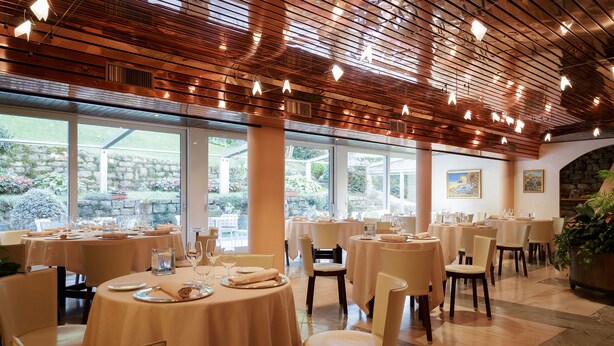 Un restaurante con mesas y sillas redondas, ventanas amplias y techo de madera.