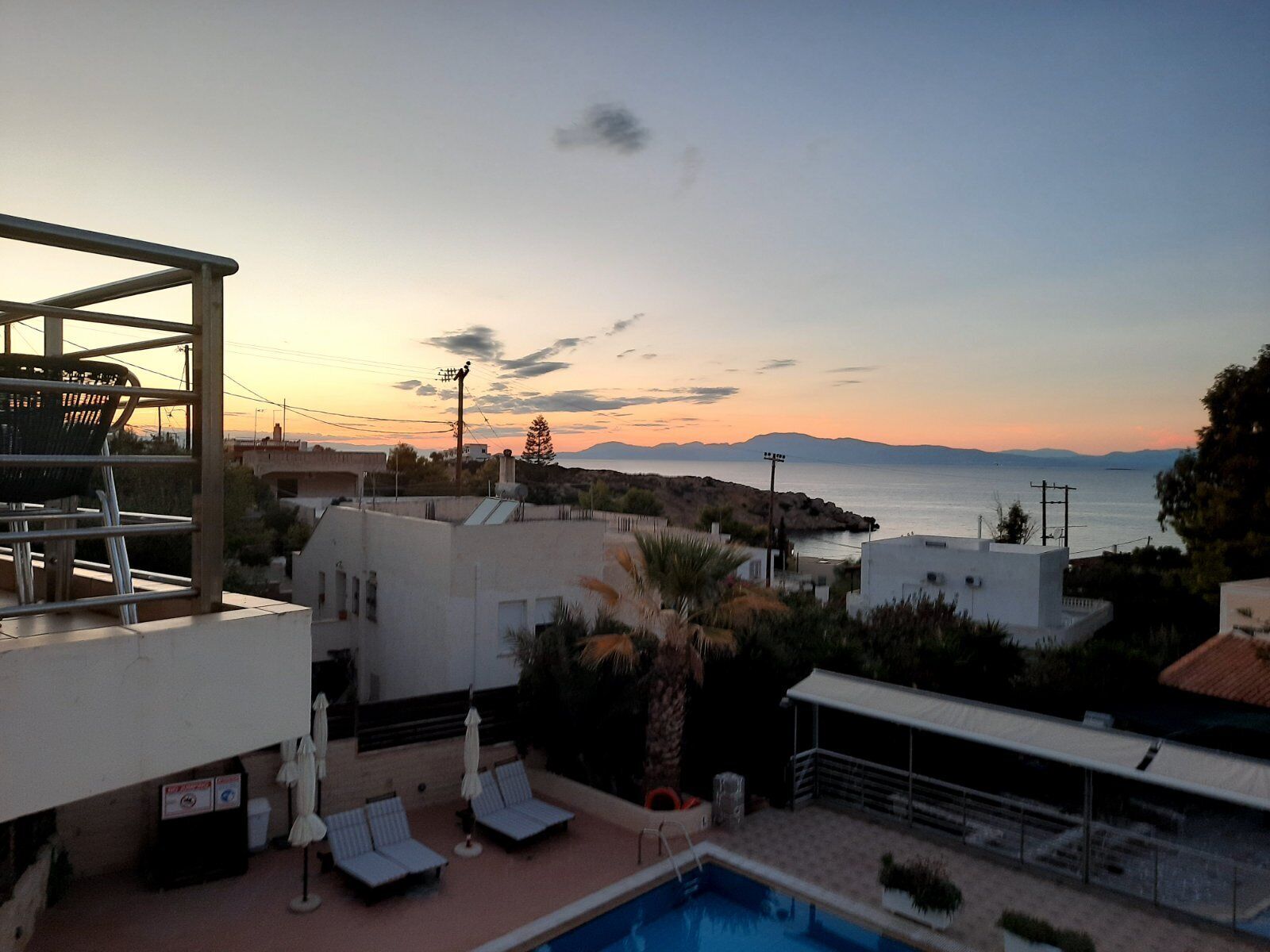A rooftop pool area with lounge chairs and umbrellas, overlooking a coastal landscape with buildings and a clear sky.