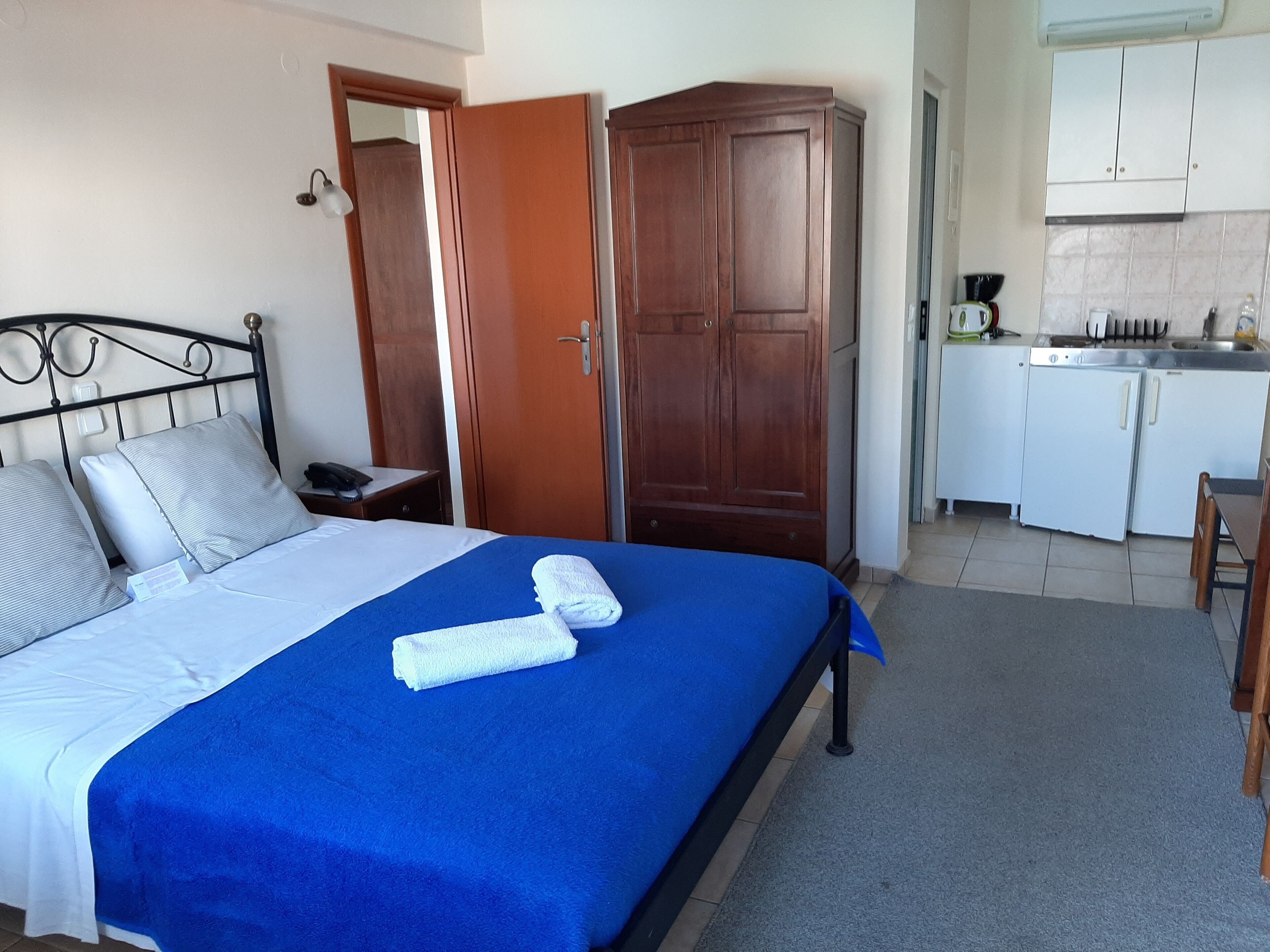 A hotel room with a bed, a wardrobe, a desk, and a kitchenette.