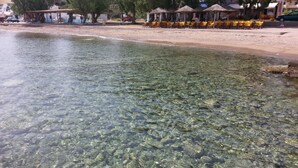 Un cuerpo de agua poco profundo y transparente con rocas visibles, una playa de arena y una fila de sombrillas y sillas amarillas, evocando un entorno costero.