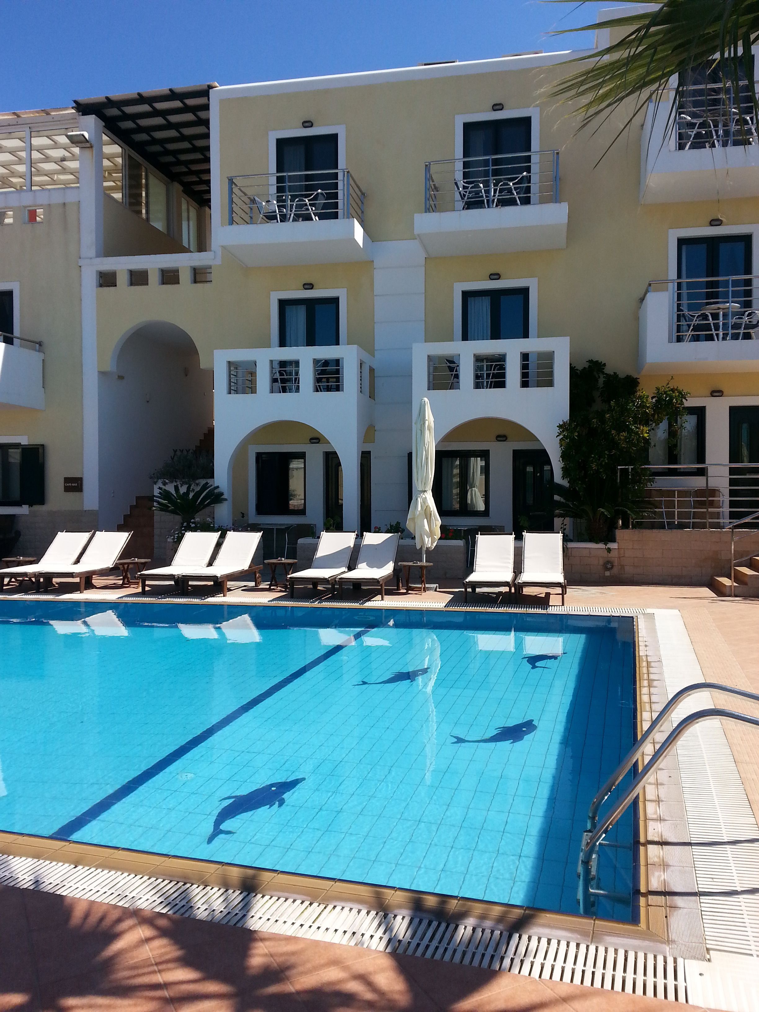 A swimming pool with lounge chairs and umbrellas, surrounded by a multi-story building with balconies.